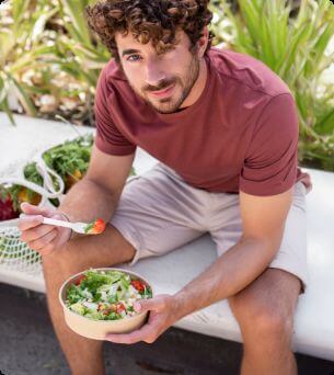 Man eet pokebowl op een bankje in de buitenlucht